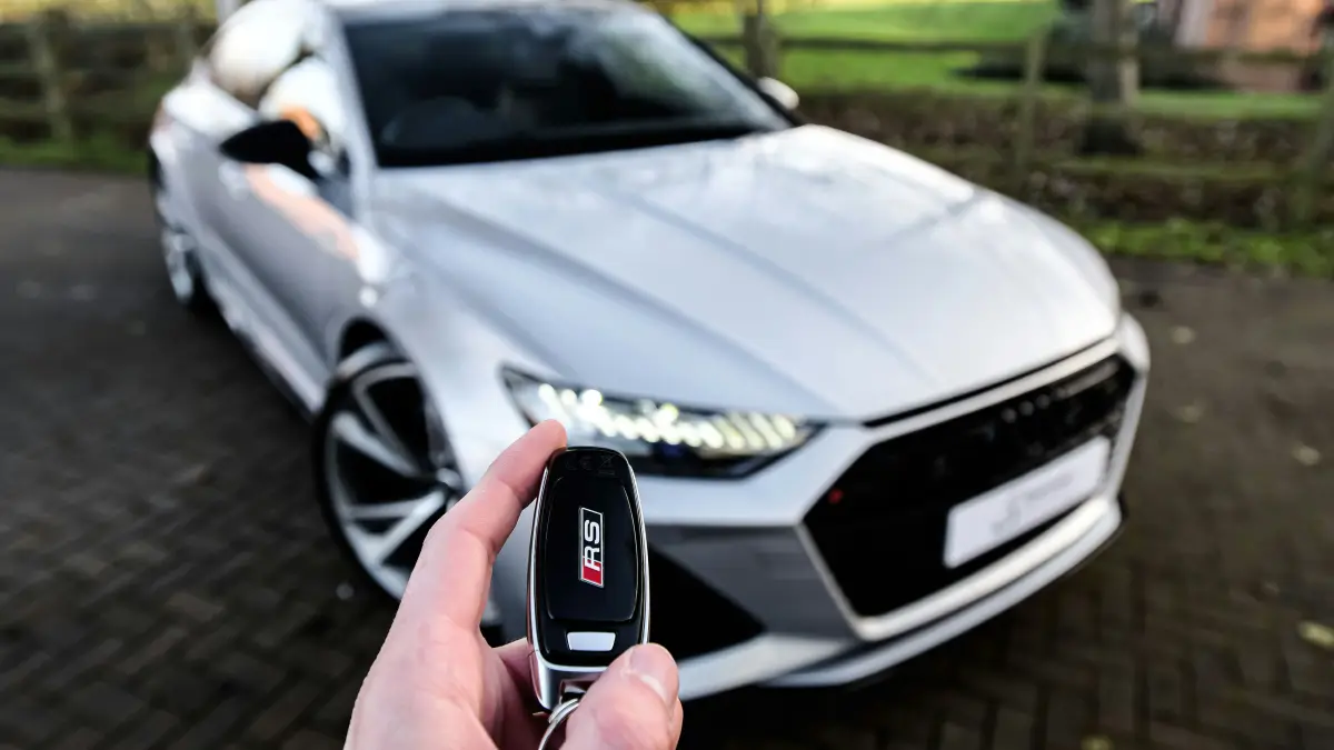 Hand hält Autoschlüssel vor einem silbernen Neuwagen